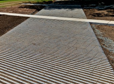 Çizgili boşlukları olan beton gri fayanslar. Çimenler boşluklarda yetişir ve otoparkın ya da kaldırımın içine sızma yüzeyi görevi görür. Ekolojik kaldırım. çakıl döşeğinde kurulum, kaldırım taşları çalışıyor