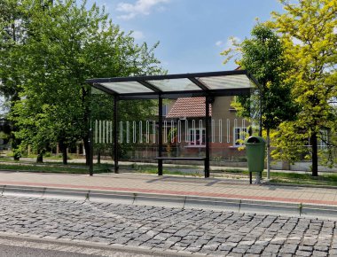 Şehir otobüs durağı. Entegre ahşap banklı cam bir sığınak. Sadece çatı ve arka duvar. Şehrin kaldırımının yanındaki caddede. Zarif kemer, istasyon, platform, çimen, çimen, dokunma
