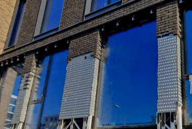 Metal bir levhada sıva olmayan tuğla işi askıya alındı. Kaldırımdaki insanların üzerine kiremit düşme tehlikesi yok. Tuğlalarla ve kaplama bantlarıyla yüzleşmek yapı taşı gibidir. ofis binası