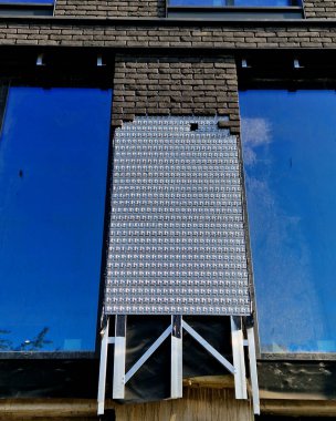 Metal bir levhada sıva olmayan tuğla işi askıya alındı. Kaldırımdaki insanların üzerine kiremit düşme tehlikesi yok. Tuğlalarla ve kaplama bantlarıyla yüzleşmek yapı taşı gibidir. ofis binası