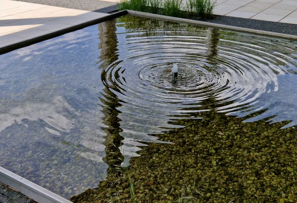 池塘平静的表面 有喷泉 使水流平静 同心圆的镜像和飞溅的声音将抚慰花园和心房 金属边 白色铺装 — 图库照片