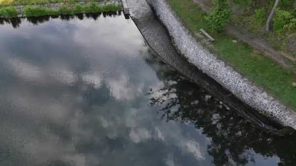 ダムの安全水路に架かっています 灰色の平らな石の自然な舗装と石の橋 擁壁の端には小さな錬鉄製の色の手すりがあります 水は流れ込み — ストック動画