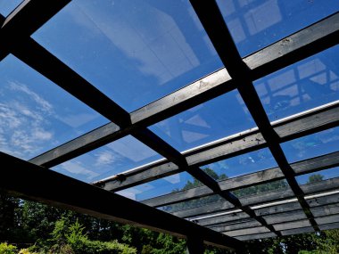 Pergola 'nın kahverengi yapışkan ahşap yapısı düz silindirik beyaz sütunlar tarafından desteklenmektedir. Çatı kiremitlerden, cam camlardan, ağaç tepesinden, kvh, akçaağaç ağacından yapılmıştır.