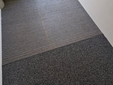 Keçeli mendil, kaset fırçası, gri alüminyum. Profiller asfalt seviyesinin altına gömülmüş. Değiştirilebilir keçeli kalemler ayakkabıları temizler ve suyu emer. Kayma riski azaldı.