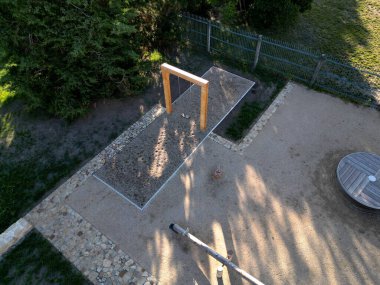 Massive wood beams in the shape of a square gate or frame, between which is a metal rod on which are swings for children. lawn by the park path. roof, metal sheet, aerial, view  footpath, lawn