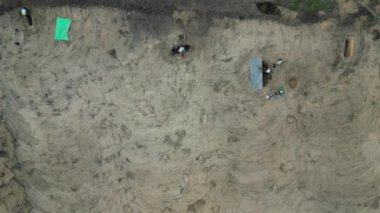 İnşaat çalışmaları arkeolojik bir araştırmayla başlar. Bir kamyon üst toprağı ithal ediyor. Arkeologlar kova dolusu bulgular kazıyorlar. Bir el arabası aylağı çukurdan çıkarır. İçinde merdiven var. 