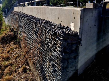 Yolun yamacını tutan çirkin beton duvar doğal taşlarla dolu bir gabion ile kaplı. Astarın görünümü daha doğal.