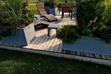 Meydandaki ağaçların altında sallanan sandalye asfaltları. Parktaki tek bir kişi için tropikal ahşaptan yapılmış ahşap sandalyeler. Kahverengi kalaslar, çatallar çelik çerçeveler, çam, kalas, açık hava.