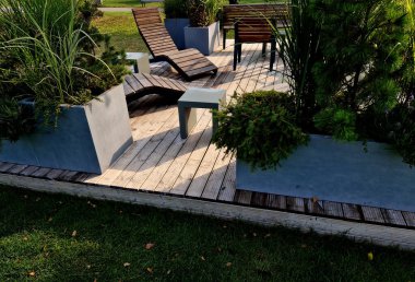 Meydandaki ağaçların altında sallanan sandalye asfaltları. Parktaki tek bir kişi için tropikal ahşaptan yapılmış ahşap sandalyeler. Kahverengi kalaslar, çatallar çelik çerçeveler, çam, kalas, açık hava.