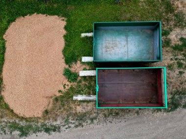 Bahçe ve parkların çimen kesikleri için yeşil teneke bir kap. Bir adam otun kalitesini ve miktarını elle kontrol eder. Bej çakıllarda bir avuç yeşil biyolojik madde. 