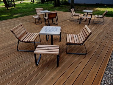 Meydandaki ağaçların altındaki kaldırımda sallanan sandalye. Parktaki tek bir kişi için tropikal ahşaptan yapılmış ahşap sandalyeler. Kahverengi kalaslar, çatallar, çelik çerçeveler ve çam ağacından yapılmışlar.