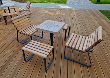 Meydandaki ağaçların altındaki kaldırımda sallanan sandalye. Parktaki tek bir kişi için tropikal ahşaptan yapılmış ahşap sandalyeler. Kahverengi kalaslar, çatallar, çelik çerçeveler ve çam ağacından yapılmışlar.