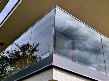 Metal paslanmaz çelik saplarla tutturulmuş cam panellerden oluşan lüks bir evin parmaklıkları. Havalı bir izlenim veriyor. Sera terası penceresinde cilalanmış metal kaplama, yansıma.