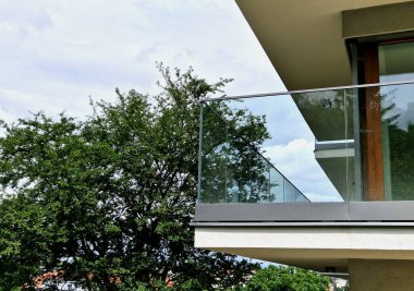 Metal paslanmaz çelik saplarla tutturulmuş cam panellerden oluşan lüks bir evin parmaklıkları. Havalı bir izlenim veriyor. Sera terası penceresinde cilalanmış metal kaplama, yansıma.