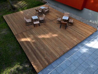 Meydandaki ağaçların altındaki kaldırımda sallanan sandalye. Parktaki tek bir kişi için tropikal ahşaptan yapılmış ahşap sandalyeler. Kahverengi kalaslar, çatallar, çelik çerçeveler ve çam ağacından yapılmışlar.