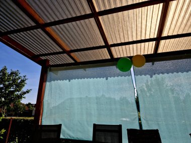 Evdeki ahşap pergola kenarlarında mavi kumaştan turkuaz perdeler ile kaplıdır. Bahçe partisinde oturmak için çok basit bir gölgeleme çözeltisi, polikarbonat, cam, kıvrımlı 