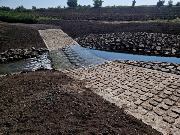 The dirt road leads across a stream that crosses river and continues when the flood road is impassable. restoration of watercourses and relocation upright drainage of fields into meandering