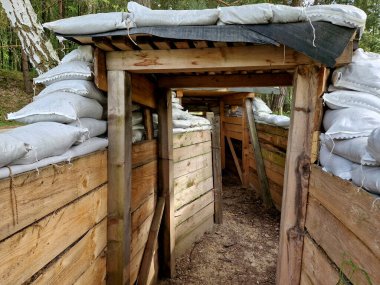 Şarapnel ve mermileri koruyor. Yerleşim yerlerinin yakınındaki toprakta havan mermileri var. Bir adam, kum torbaları arasındaki bir gözetleme deliğinden düşman birliklerine ateş ettiği yeri gösterir. Ahşap yapısı olan bir siper..