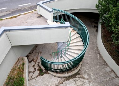 Kalın bir borunun etrafındaki gri spiral merdiven köprünün çatalına ya da bir binaya çıkıyor. Tırabzan dikey çarşaftan, ağaçtan, çalılıktan yapılmıştır.