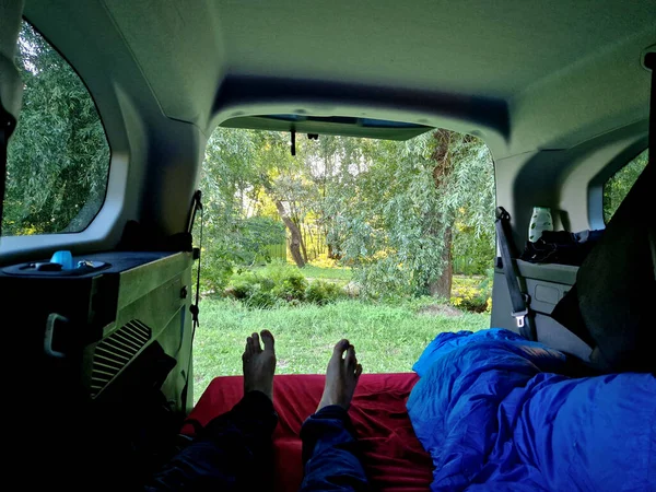 a man lies inside the trunk of a car on a mattress after spending the night outside in nature. sleeping in a car is prohibited in many countries. fines are issued for the topic of camping