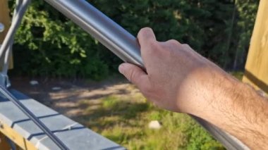 Bir adam tırabzanı tutar ve eliyle spiral bir merdivenin çubuğunu okşar. Gözcüye giderken paslanmaz çelik sapın pürüzsüz yüzeyini parlat.