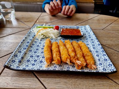 Çocuk en sevdiği karidesi dört gözle bekliyor. Ekmek kırıntılarında kızartılmış karides ve Akdeniz usulü salata. Tahta masa, el ele tutuşarak.