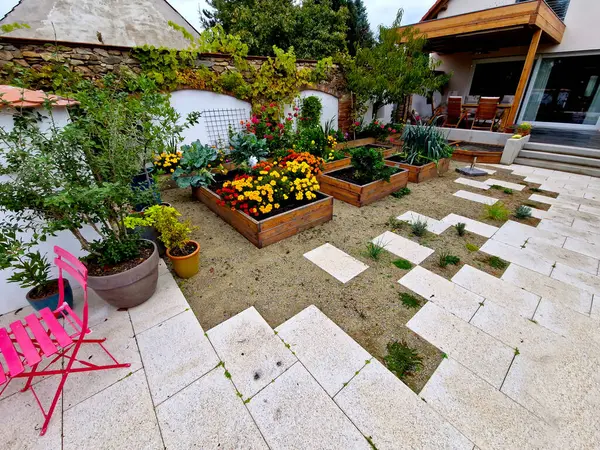 corner of the family garden with several beds bordered by boards. there is compacted sand around and the paving irregularly jaggedly rises into the mortar. flowering beds with annuals