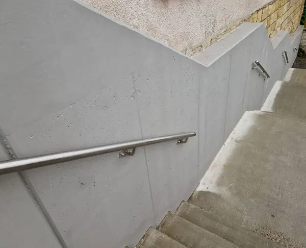 a staircase with concrete sides at a public building. the safe staircase has two handrails, one with a reduced height for children under 12 at the entrance to the school, brick, black, red. forgery