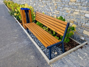 Apartman binasının yanındaki bankta oturuyor. Zarif banklar ve ahşap tahtalarla kaplı kare bir çöp sepeti. Evi kesilmiş kiremitlerle kaplamak.