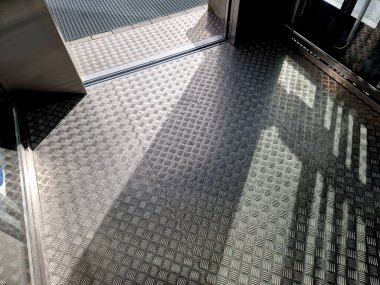 Açık hava asansörü. Genişletilmiş metalden yapılmış kaymayan metal zemin. Metal ızgara örgü ayakkabı temizleme paspası. İç mekan, güneşli, zemin, dış görünüş