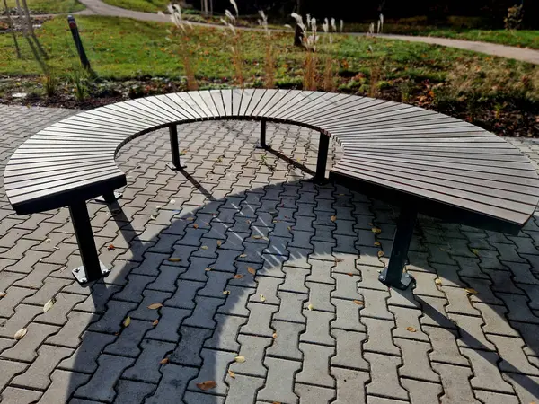 stock image circular bench made of brown-red teak wood. tropical impregnated podia boards for sunbathing visitors in the park. spiral shape, snail shells. trowel base in lawn, tree, trunk, grass