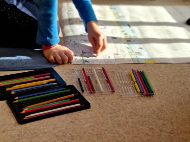  Çocuk bir dairede yerde oturuyor ve fantezi dünyalarını büyük bir kağıt parçasına çiziyor. Madenler ve 2D 'deki mağaralar. Elimde bir sürü boya kalemi var..