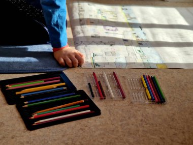  Çocuk bir dairede yerde oturuyor ve fantezi dünyalarını büyük bir kağıt parçasına çiziyor. Madenler ve 2D 'deki mağaralar. Elimde bir sürü boya kalemi var..