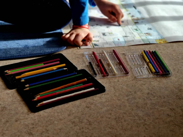 boy sits on the floor in an apartment and draws his fantasy worlds out of cubes on a large piece of paper. mines and caving in 2d. lots of crayons in cartridges right at hand.