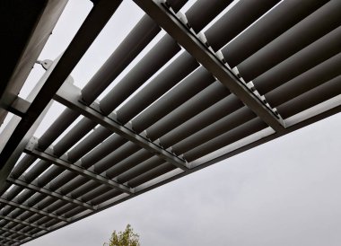Otobüs durağının metal inşaatı, çardak pergola barınağı. Çatı ve duvarlar tırmanma tesisleri için bir halat ağıyla örülmüş. Paslanmaz çelik eşleşmelerle sabitlenmiş. siyah blok şekilli tünel,