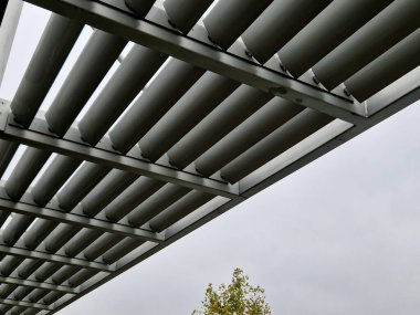 Otobüs durağının metal inşaatı, çardak pergola barınağı. Çatı ve duvarlar tırmanma tesisleri için bir halat ağıyla örülmüş. Paslanmaz çelik eşleşmelerle sabitlenmiş. siyah blok şekilli tünel,