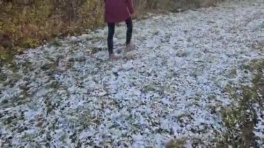 Pencereden bahçeye sabah manzarası. Terasa ve ahşap pergola üzerine yavaşça kar yağar. Bir kadın karlı çimlerde yürüyor.