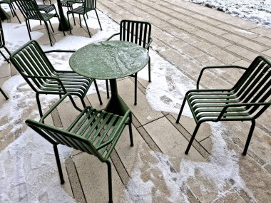 at a work meeting, terrace of a cafe on the sidewalk in the administrative zone. black mesh chairs and square wooden tables. a paper cup with coffee and a mobile phone. croissant on a plate. foot over