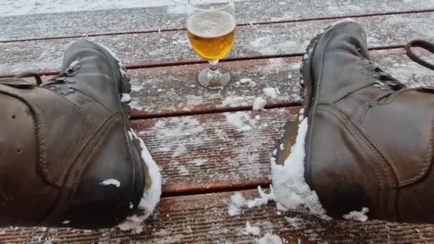 男はビールを一杯飲んで 雪で覆われた冬の真ん中に 彼の健康を祝う 足にグラスをつけて 自然の中で豊かな味わいを持つ黄金色の金色 — ストック動画