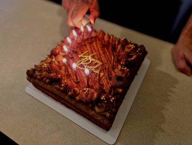 Çikolata malzemelerinden yapılmış bir pastanın her gece hazırlanmış görüntüsü. Mumlar, plastik harflerden yapılmış bir yazının etrafını sarar. 15 mum yakarak ailelerden bir çakmak yakarak.