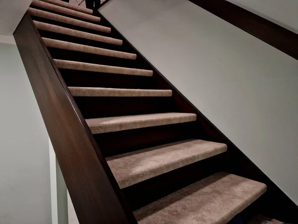 the staircase in the house is lined with carpeted stairs. the carpet is stuck on the stairs. the side panel is made of stained solid wood. there is no railing, so the room is more spacious