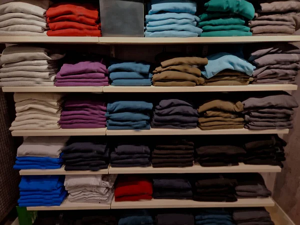 the wardrobe with shelves is clearly divided by color and type of clothing. shirts with collars in a palette of colors and t-shirts and hoodies for the customer to choose according to taste