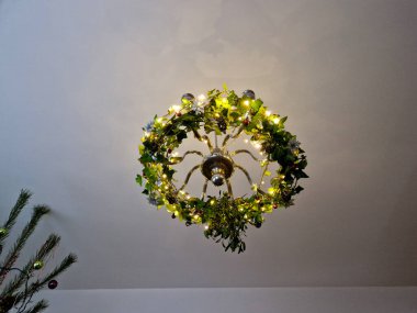 Sekiz kollu eski bir avize. Gümüş renkli, ladin konisi şeklinde ampulleri ve altta bir topu var. Perdeli beyaz oda. Alt manzara. Mum şekilli, örümcekli, sarılan, öne çıkan, krom