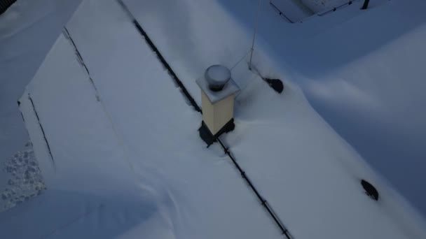 一个冒烟的烟囱 在雪天的屋顶上也有一道屏障 以防止雪滑落 金属棒支撑着这一层 用无人驾驶飞机检查烟囱里的烟道气可以保护环境 — 图库视频影像