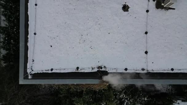 一个冒烟的烟囱 在雪天的屋顶上也有一道屏障 以防止雪滑落 金属棒支撑着这一层 用无人驾驶飞机检查烟囱里的烟道气可以保护环境 — 图库视频影像