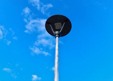 Gri paslanmaz çelik sütun daire şekli. Şeffaf bir kapağı ve LED lambaları olan bir lamba. Sokak lambasının üstünde küçük bir güneş paneli var. halka açık park