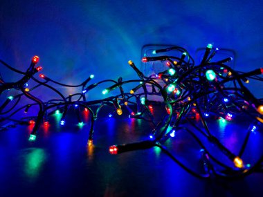 Koyu mavi arka plandaki ışık zincirleri gece yıldızlı bir gökyüzünü andırıyor. Noel için aydınlatılmış süslemelerle sergi standı, makara, düğüm, düğüm, top