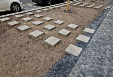 Basamaklar çiçek tarhının ortasına çıkar. Ağacın etrafında damlayan bir boru var. Toprak yüzeyinde otomatik sulama hortumu, dama tahtası ızgarasında kare beton fayanslar