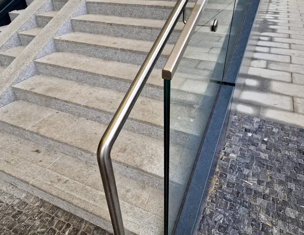the edge of the glued glass of the railing covered by a U-shaped strip. transparent fillings of the railing made of shiny stainless steel tube bent. step into the building