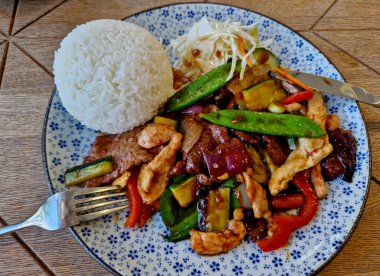 Kızarmış et, bezelye kabuğu ve pirinç yığınıyla Szechuan usulü tavuk. Çiçek tabağı, lahana salatası ve kırmızı biber. Vietnam tarzında renkli sağlıklı yiyecekler. Manzaralı.